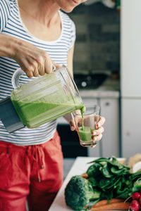 Caucasian woman pours smoothie into a glass. vegetable drink. healthy eating concept. 