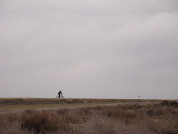 Man cycling on field against sky