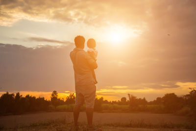 Rear view of man standing on field against sky during sunset