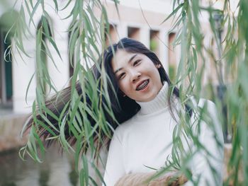 Portrait of smiling young woman standing by plants in park