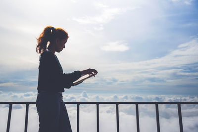 Side view of woman reading book against cloudy sky