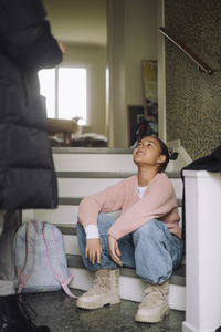 Girl looking at father while sitting with bag on steps at home