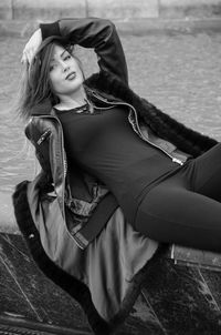 Portrait of young woman relaxing on retaining wall by river