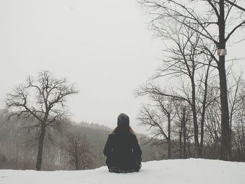 Rear view of young woman sitting on snow covered mountain against sky in forest