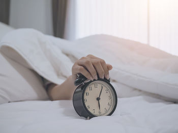 Woman lying on bed while holding alarm clock