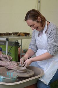 Smiling mature woman shaping clay on pottery wheel by cropped man in workshop