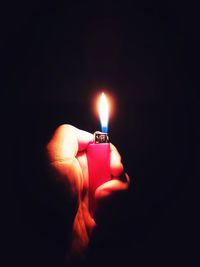 Close-up of hand holding lit candle in darkroom