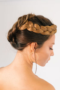 Side view of beautiful young female model with elegant braided hairstyle and makeup and with golden hoop earrings against white background