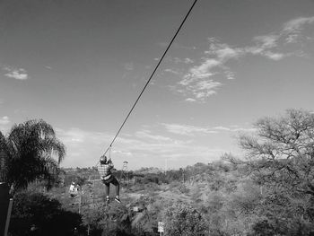Full length rear view of person zip lining over landscape against sky