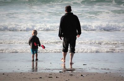 Day at the beach. father and son walking towards waves.