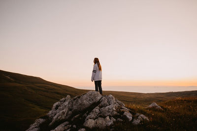 Young woman standing on rock at field against clear sky