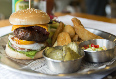 Close-up of hamburger with chips by salad and pickles served in plate on table