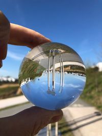 Close-up of hand holding crystal ball against blue sky