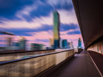 Blurred motion of train in city against sky during sunset