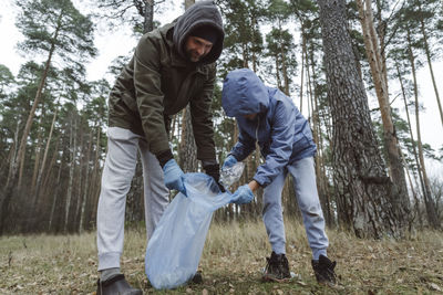 Father and son collecting plastic waste in garbage bag at forest
