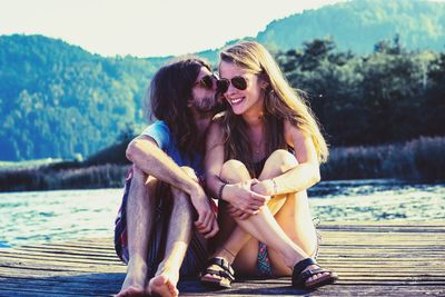 Portrait of smiling young woman sitting by lake against sky