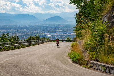 Rear view of man riding bicycle on road against mountains