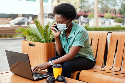 Woman wearing mask talking over mobile phone while sitting at cafe