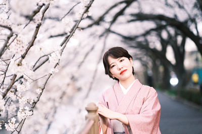 Portrait of young woman standing against blurred background