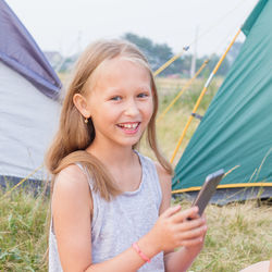 Portrait of smiling girl holding mobile phone outdoors