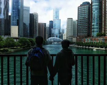 Rear view of couple holding hands against river and buildings