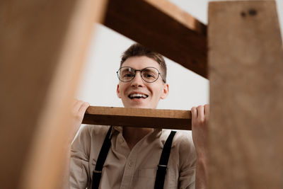 Portrait of smiling young man sitting with ladder against white background