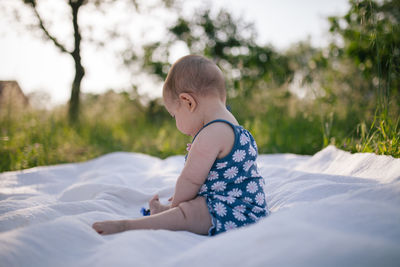 Side view of baby girl sitting on blanket at park