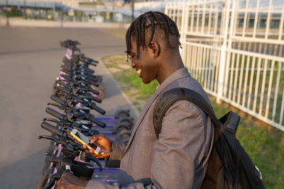 Smiling businessman using smart phone in front of electric push scooter station