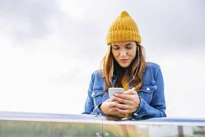 Smiling young woman wearing yellow cap looking at cell phone