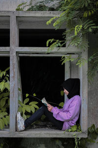 Side view of woman sitting by window