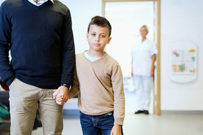 Portrait of boy holding father's hand with nurse in background at orthopedic clinic