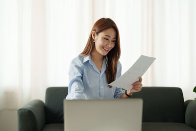 Young woman using laptop while sitting on sofa at home