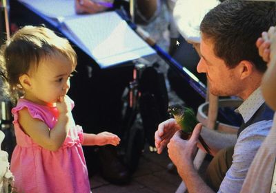 Girl looking at bird perching on man hand