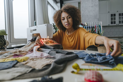 Young fashion designer sitting with clothes and sewing machine at table