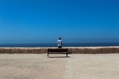 Rear view of man looking at sea against clear blue sky