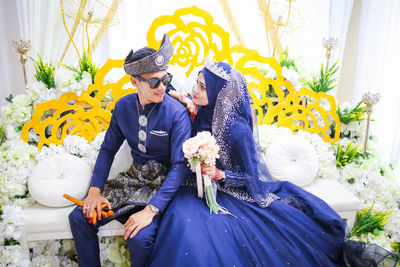 Bride and groom looking at each other while sitting on sofa