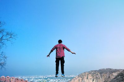 Rear view of levitating in mid-air against clear blue sky