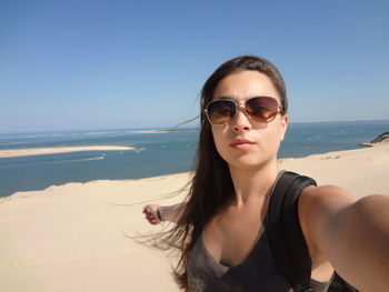 Portrait of young woman wearing sunglasses at beach against sky