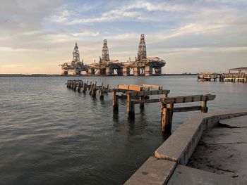 Offshore platform in sea against cloudy sky during sunset