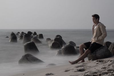 Man sitting at beach against clear sky