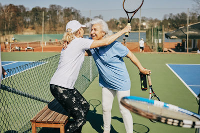 Happy female senior friends greeting at tennis court during summer