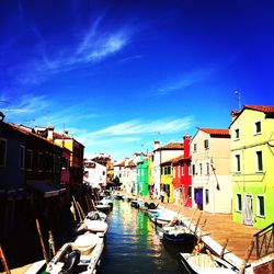 Boats moored in canal amidst buildings against blue sky