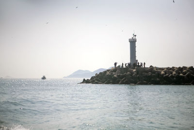 View of people surrounding lighthouse in sea against clear sky
