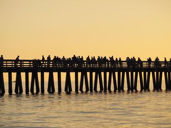 Silhouette people on pier over sea against clear sky during sunset