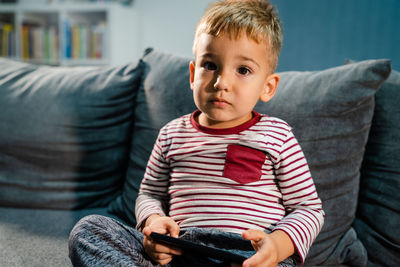 Portrait of boy holding mobile phone while sitting on sofa at home