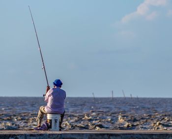 Rear view of man fishing on beach against sky
