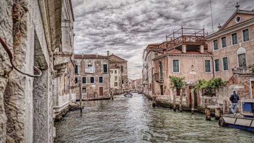 View of canal and buildings against cloudy sky