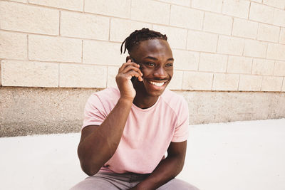 Smiling man talking on mobile phone against wall