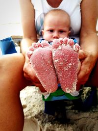 Midsection of mother holding baby boy with sandy feet at beach