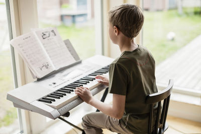 Rear view of boy playing piano at home
